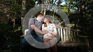 Happy pregnant woman and her husband in the forest. Man caressing woman's belly