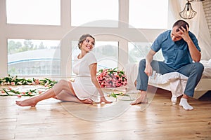 Happy pregnant woman with her husband are holding and listening to baby in belly and setting on living room`s floor at home, preg