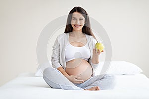 Happy pregnant woman holding apple and touching belly