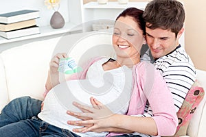 Happy pregnant woman holding baby shoes at home