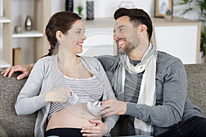 happy pregnant woman holding baby shoes and husband