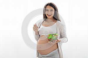 Happy pregnant woman holding bowl with fresh salad and fork