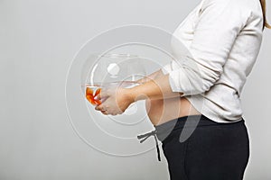 Happy pregnant woman holding a fishbowl with a goldfish in her h