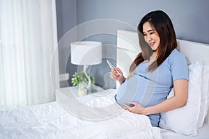 Happy pregnant woman holding and looking ultrasound scan photo on bed