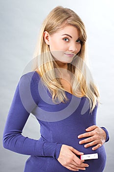 Happy pregnant woman holding pregnancy test and touching her belly