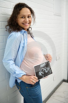 Happy pregnant woman holding ultrasound scan of her baby. Pregnancy. Obstetrics and gynecology concept. Health care