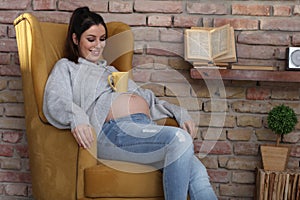 Happy pregnant woman at home relaxing in armchair