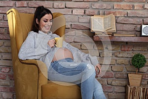 Happy pregnant woman at home relaxing in armchair