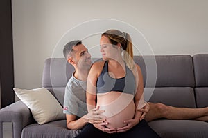 Happy pregnant woman with husband looking at each other and expecting baby at home