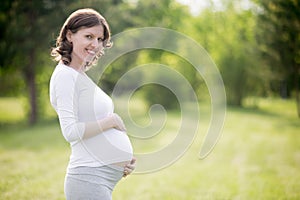 Happy pregnant woman on late pregnancy stage posing in park