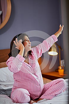 Happy pregnant woman listen to music with headphones while sitting on the bed at home