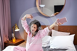 Happy pregnant woman listen to music with headphones while sitting on the bed at home