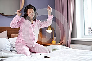 Happy pregnant woman listen to music with headphones while sitting on the bed at home