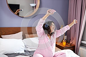 Happy pregnant woman listen to music with headphones while sitting on the bed at home