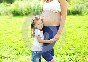 Happy pregnant woman, little child daughter listens tummy mother in summer