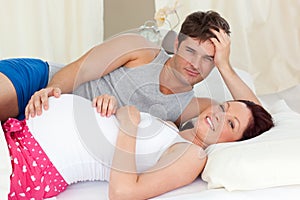 Happy pregnant woman lying on bed with her husband