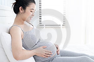 Happy pregnant woman lying on bed and touching her belly at home.