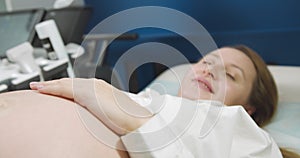 Happy pregnant woman lying down getting ultrasound investigation. Doctor fertility specialist uses ultrasound equipment