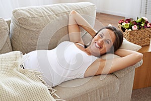 Happy pregnant woman lying down on sofa with hands behind her he