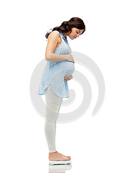 Happy pregnant woman measuring weight on scales