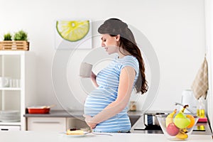 Happy pregnant woman with mug and cake at home