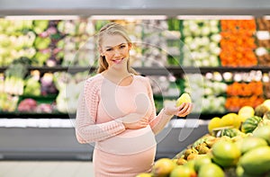 Happy pregnant woman with pear at grocery store