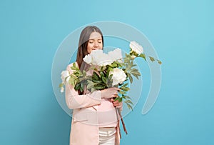happy pregnant woman in pink t-shirt on blue background holding a bouquet of flowers