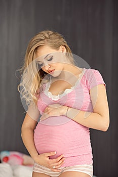 Happy pregnant woman posing in pink blouse. Attractive young blonde glamour girl at home.