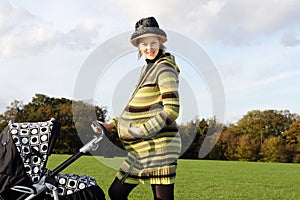 Happy pregnant woman pushing pushchair in the park