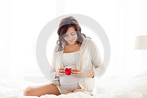 Happy pregnant woman with red heart in bed at home