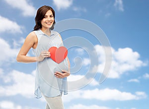 Happy pregnant woman with red heart touching belly