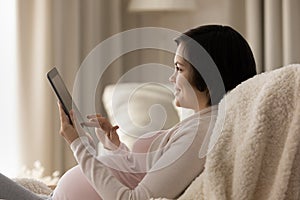 Happy pregnant woman relax in chair using tablet