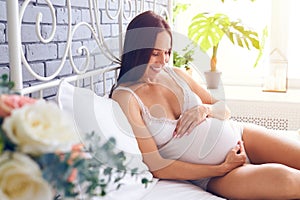 Happy pregnant woman is resting at home on bed