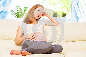 Happy pregnant woman is resting at home on sofa