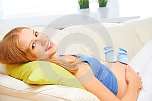 Happy pregnant woman is resting at home on sofa and holding a bl