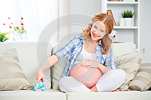 Happy pregnant woman is resting at home on sofa and holding a bl
