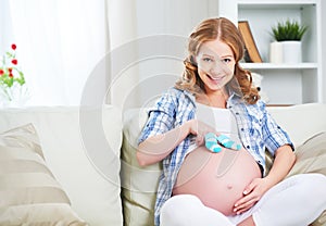 Happy pregnant woman is resting at home on sofa and holding a bl