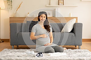 Happy Pregnant Woman sit on carpet in front of sofa and stroking big belly with baby stuff prepare for love at cozy home,Pregnancy