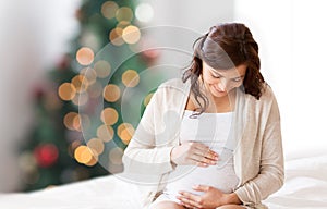 Happy pregnant woman sitting on bed at christmas