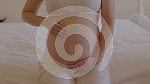 Happy Pregnant Woman sitting on bed holding and stroking her big belly at home,Pregnancy of young woman enjoying with future life,