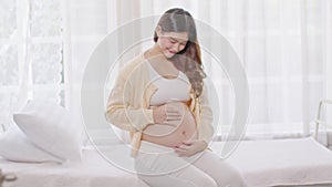 Happy Pregnant Woman sitting on bed holding and stroking her big belly at home,Pregnancy of young woman enjoying with future life