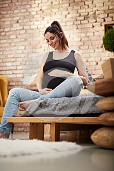 Happy pregnant woman sitting on bed at home