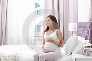 Happy pregnant woman sitting on bed