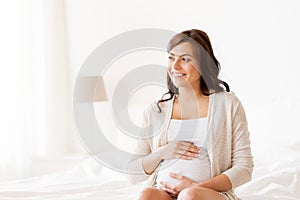 Happy pregnant woman sitting on bed at home