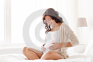 Happy pregnant woman sitting on bed at home photo