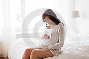 Happy pregnant woman sitting on bed at home