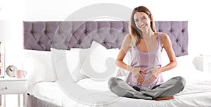 Happy pregnant woman sitting in bed at home, space for text. Banner design