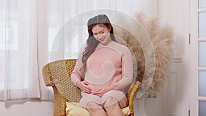 Happy Pregnant Woman sitting on couch holding and stroking her big belly at cozy home,Pregnancy of young woman enjoying with