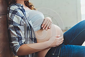 Happy pregnant woman sitting on the floor and touching her belly at home