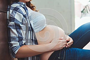 Happy pregnant woman sitting on the floor and touching her belly at home